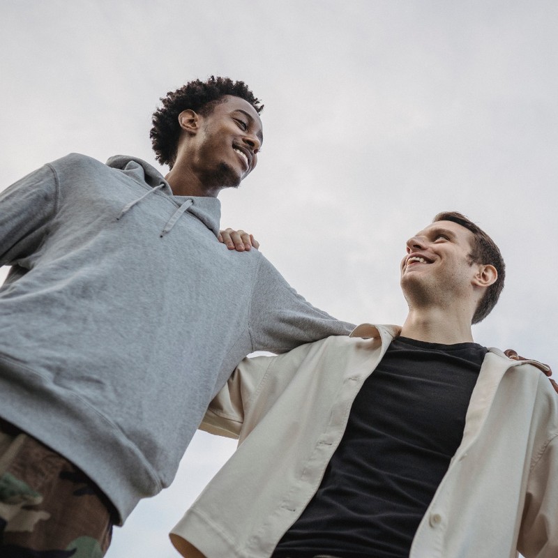 Two men stand with their arms around the other’s shoulders.