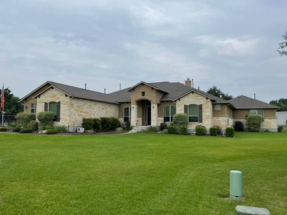 A modern stone home with brown shingles and a green front yard.