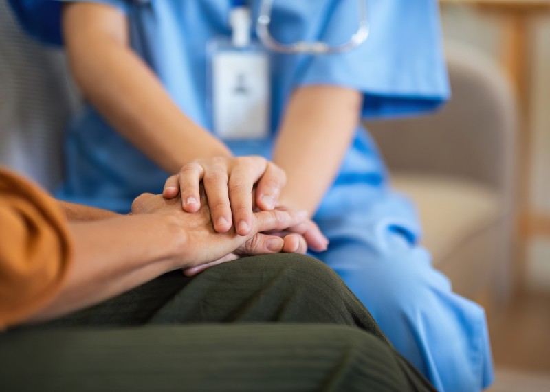 A hospice nurse holds the hand of a patient.