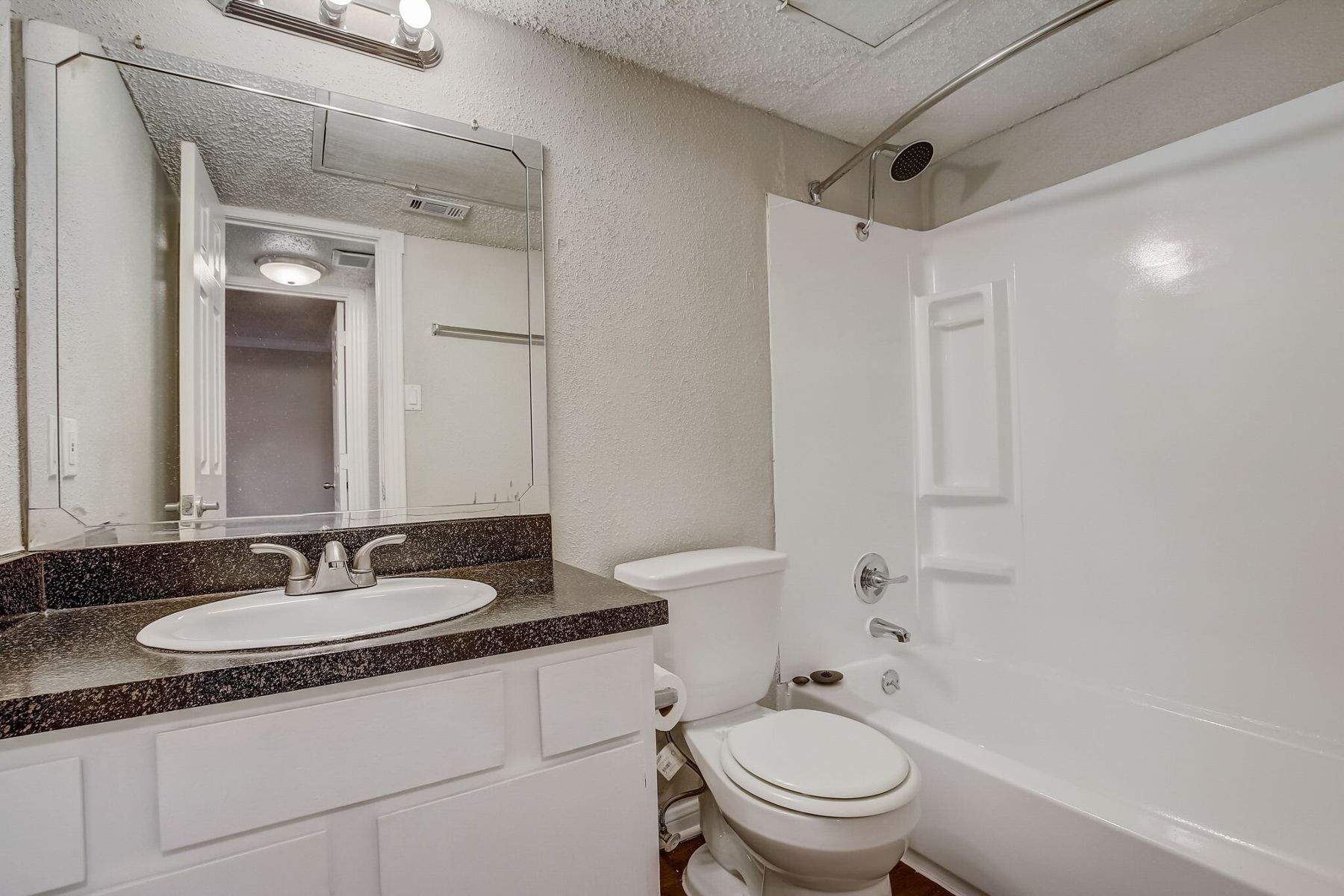 The bathroom of an apartment with white cabinetry and a dark granite sink countertop.