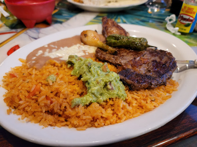 A plate of steak, guacamole, fried rice, and refried beans