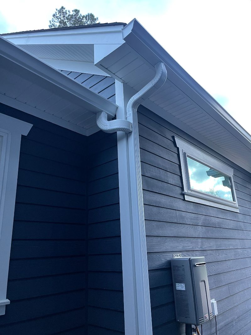 A white gutter and downspout system on a gray home.