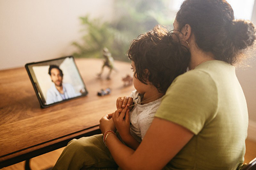  A woman holds a young child while watching a tablet.