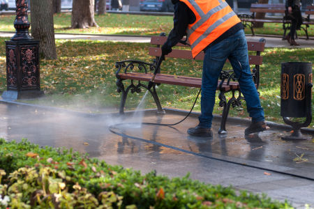 A man pressure washes a concrete sidewalk.