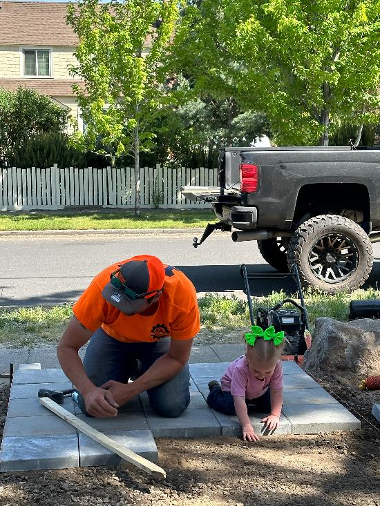 Aman and little girl work together to lay stone pavers for a walkway.