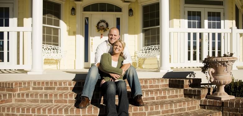 A man and woman smile while sitting on the steps of their home.