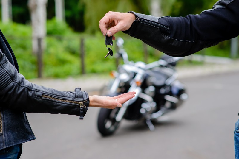 A man hands a woman the keys to a new motorcycle with the cycle in the background.