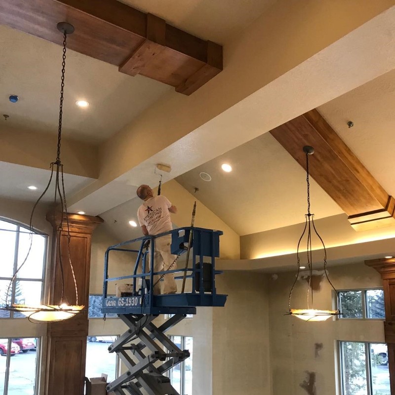 A man on a lift paints a vaulted ceiling. 