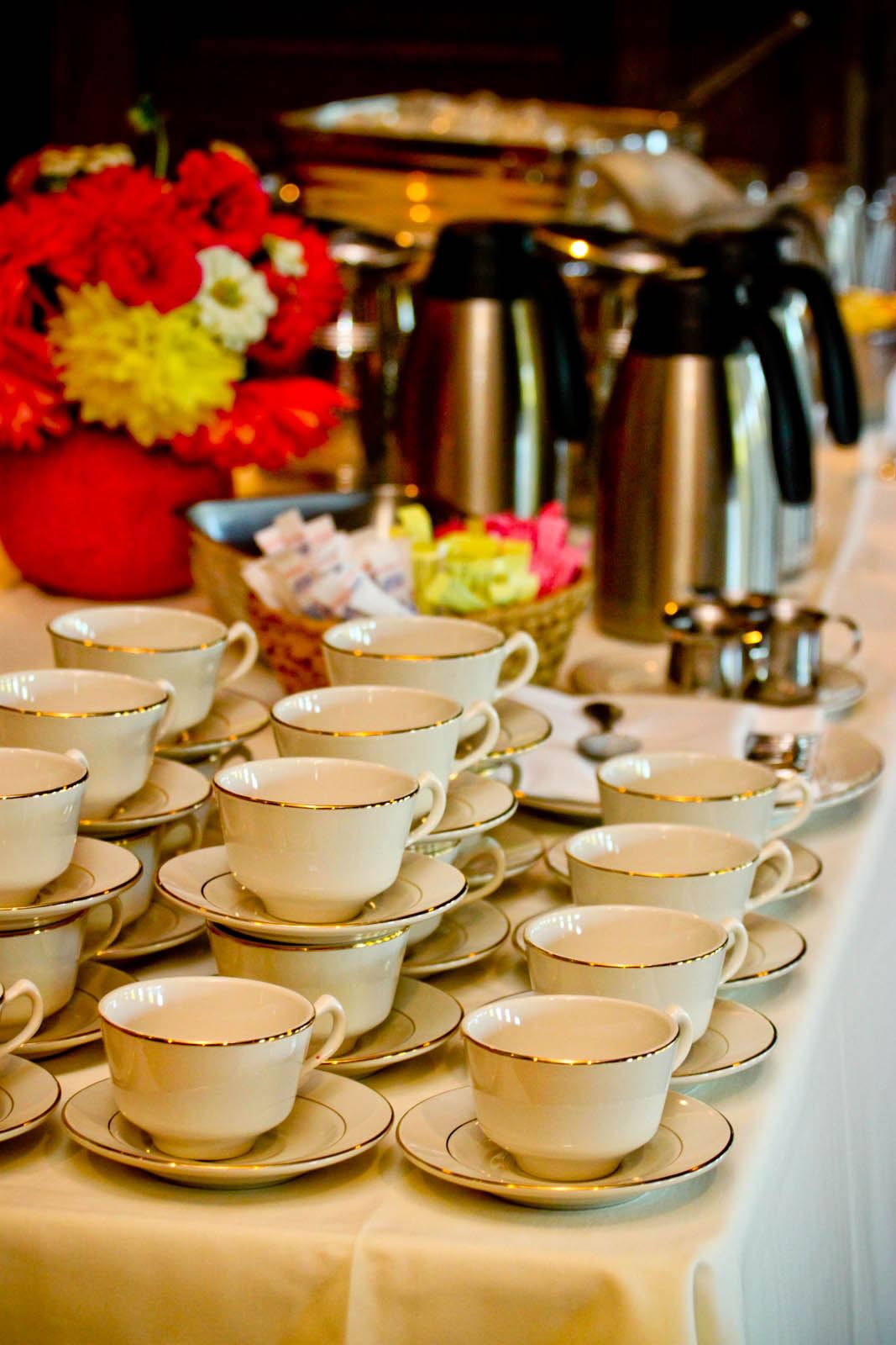 Coffee and tea cups stacked neatly on a buffet table with carafes in the background