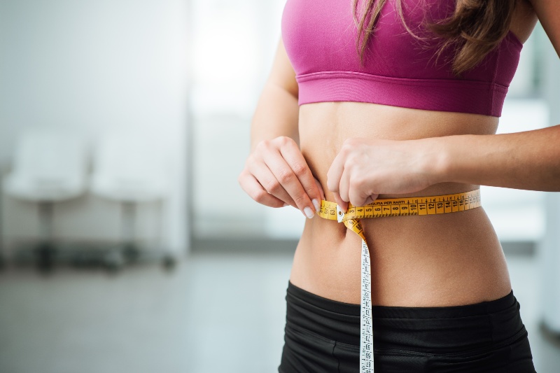 A woman measures her waist with a tape measure.