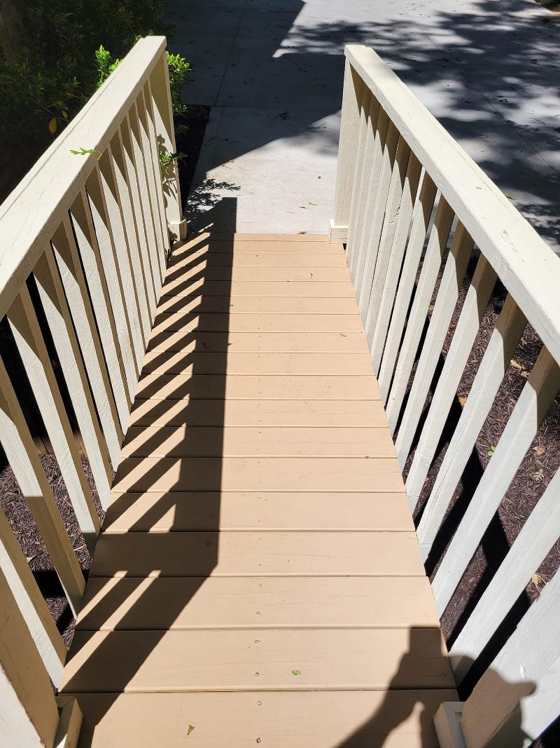 A wooden walkway and railing leading to a sidewalk.