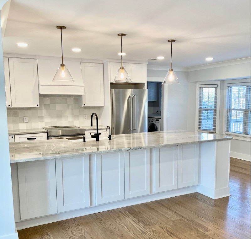 A kitchen scene with white cabinetry and a granite countertop island.