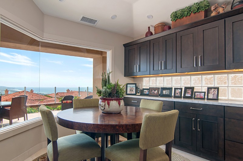 View out kitchen bay window showing dark cabinets, breakfast nook, roofs of neighboring homes