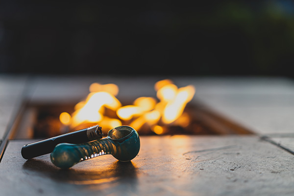 marijuana pipe with a lighter in front of a fire pit
