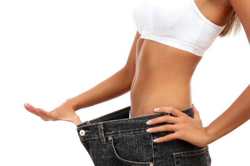 A woman shows off her loose jeans after weight loss.