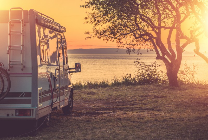 A small motor home sits parked near the edge of a lake at sundown.