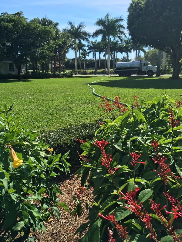  A long hose extends across a yard to a pumper truck.