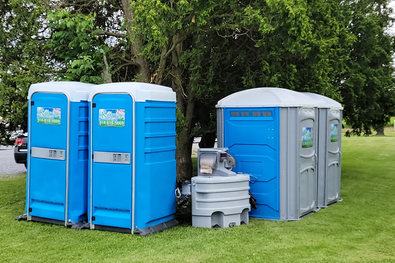 Four portable toilets with a portable sink situated in the middle.