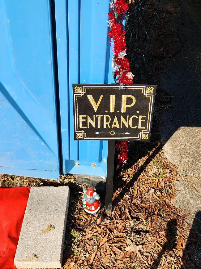 A small gnome sits on the ground in front of a portable toilet.