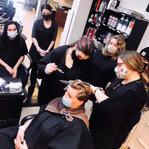 Three students apply hair color on a girl with two others looking on.