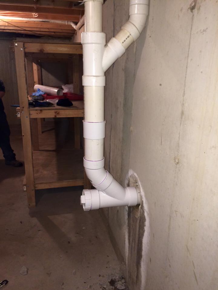 A white PVC pipe leads into a basement wall. 