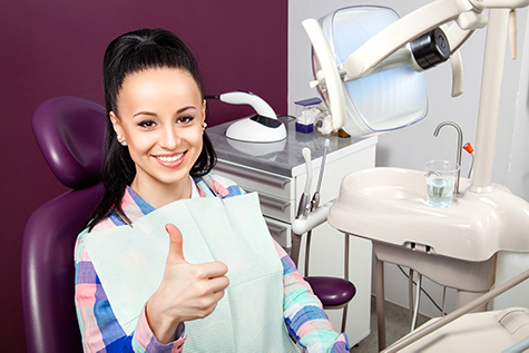 Young woman sits in a dentist chair and gives a thumbs-up.