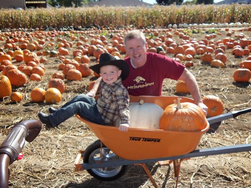 Tom Rush is seen with a young child in a wheelbarrow in front of a pumpkin patch.