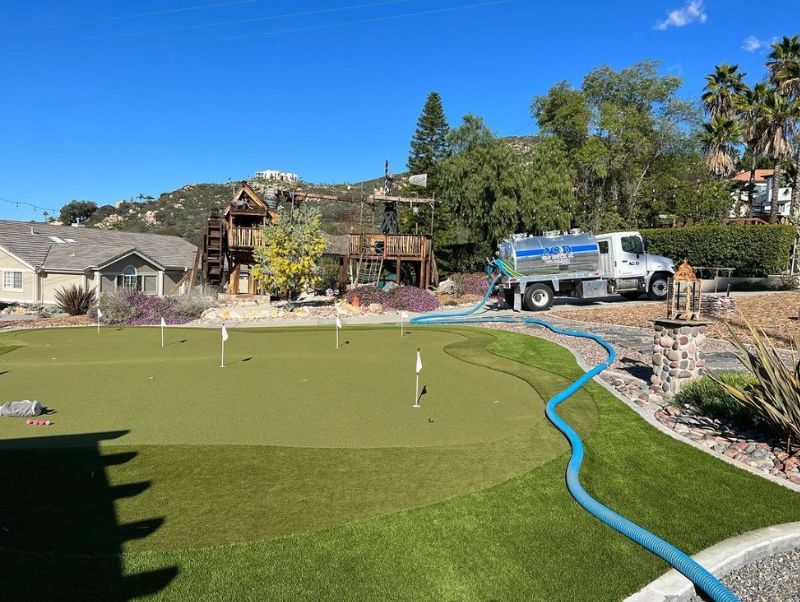 A pumper trucks has a long, blue hose stretched out over a grassy lawn.