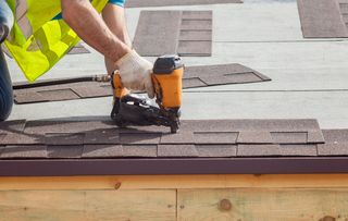 A worker installs shingles on a roof