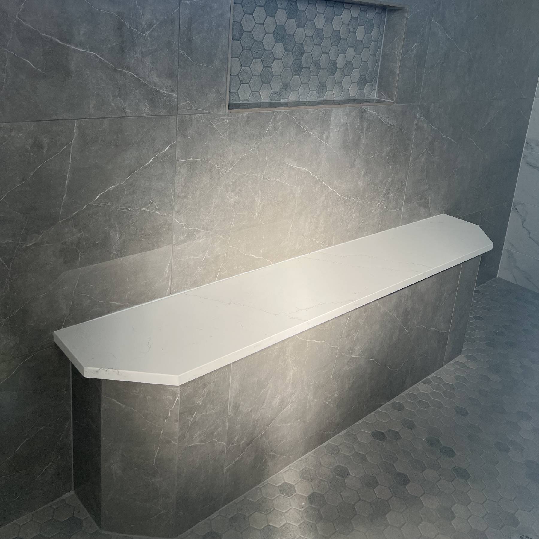 Built-in bench and recessed shower shelf in a large, gray-tiled shower.