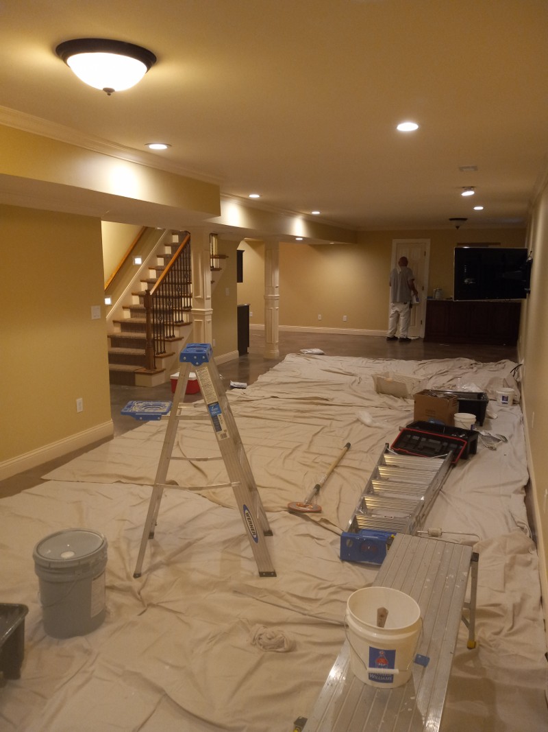 A painter works on painting an empty room with a drop cloth on the floor.