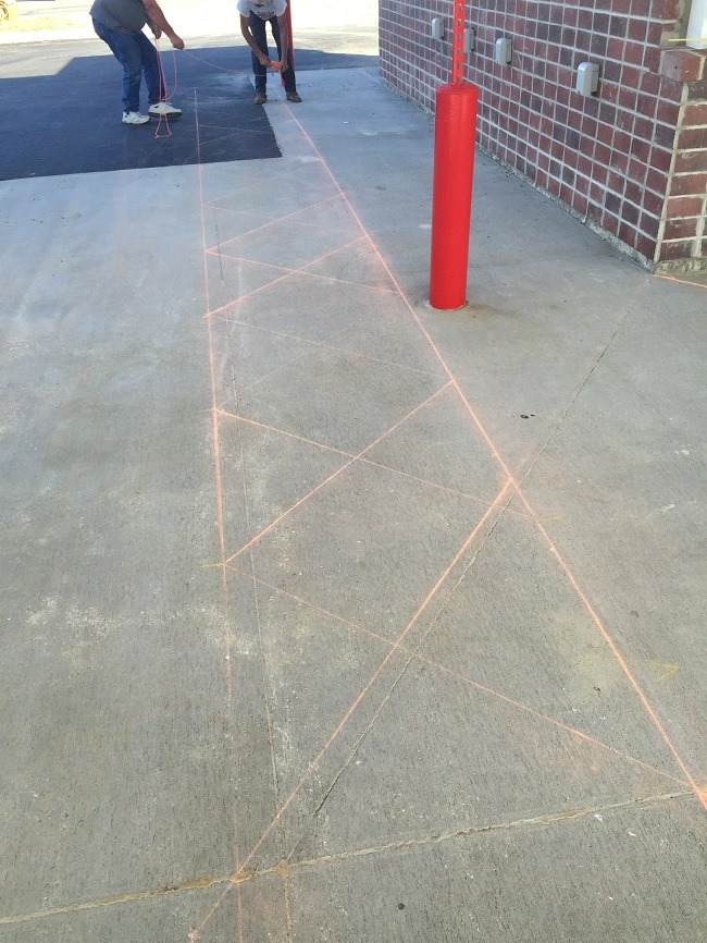 Two men inspect a newly laid section of asphalt.