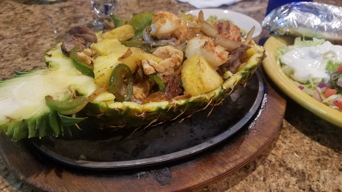 A pineapple boat containing grilled shrimp, green peppers, and pineapple chunks.