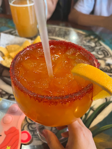 A salted-rim orange margarita with a slice of lemon.