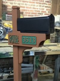 A black mailbox sits on a brown post with greenand gold address lettering.