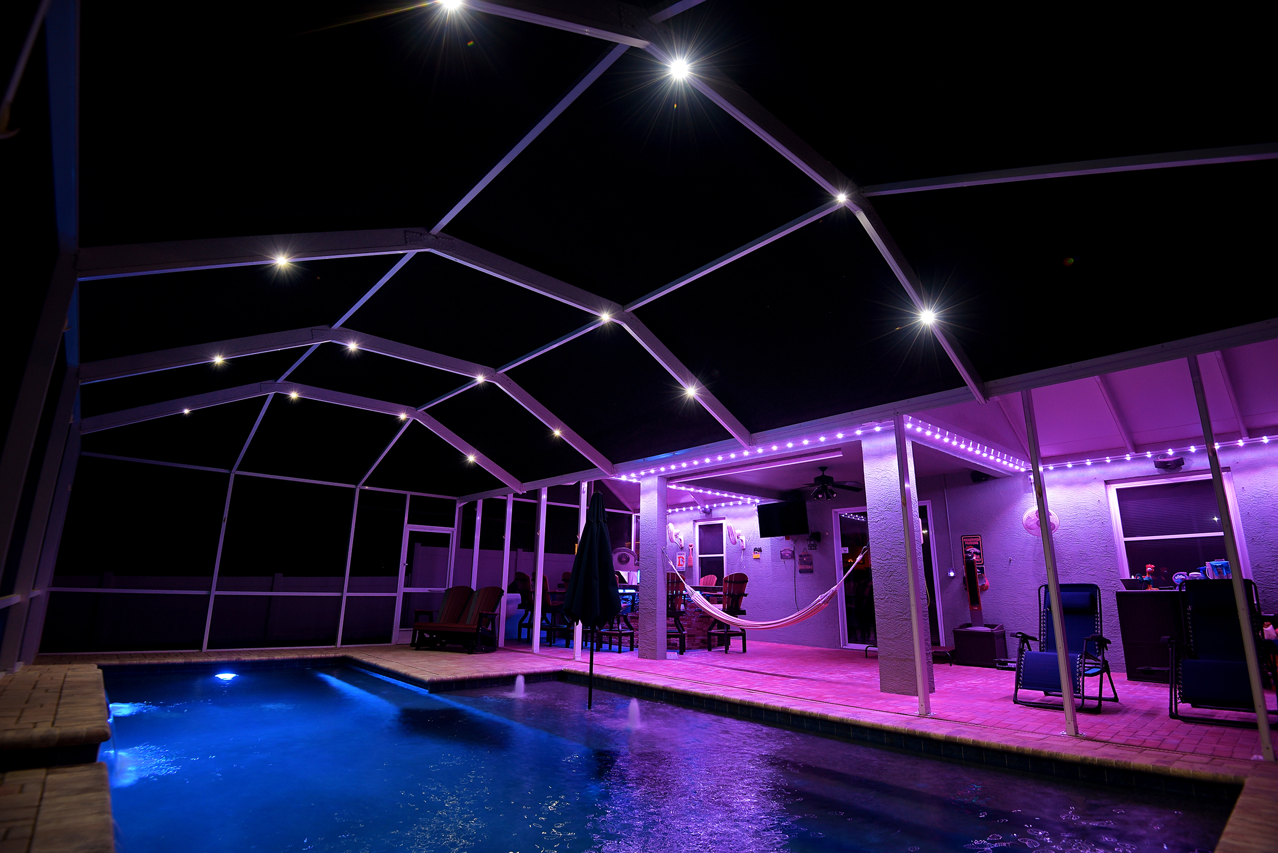 Enclosed pool house at dusk with overhead lighting and green accent lighting around the base.