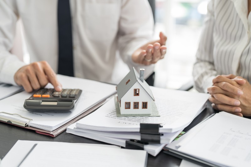 insurance agent with calculator model home on desk