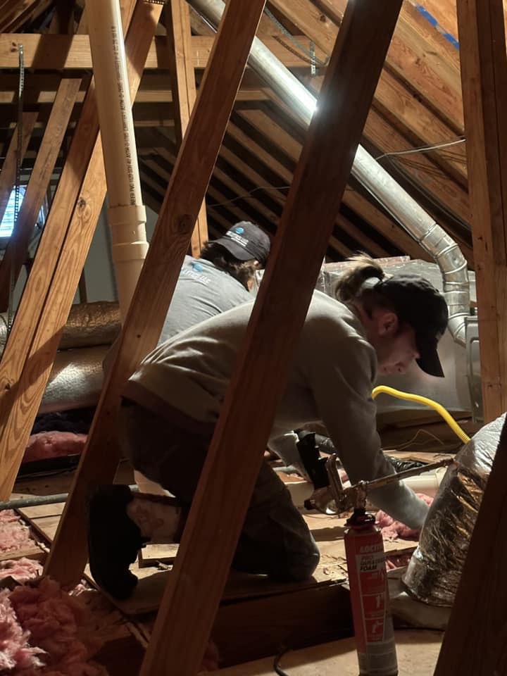 A man installs rolled insulation in an attic.