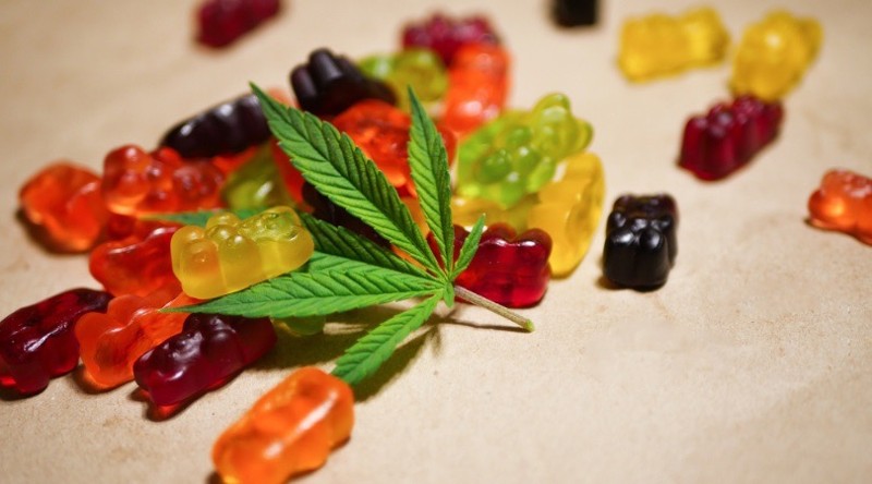 Multi-colored gummy bears and cannabis leaf lie on a tan counter-top