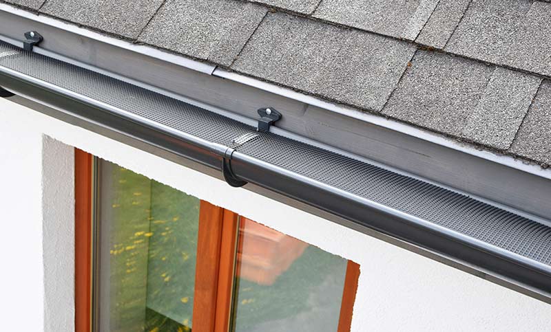 A silver gutter guard attached to a gutter.