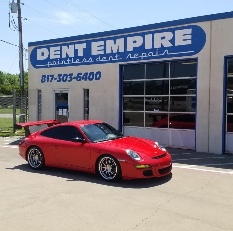 A red Porsche is parked in front of the Dent Empire repair shop. 