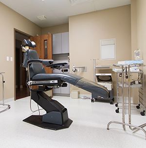 dental exam chair, black, silver tables and tools surround