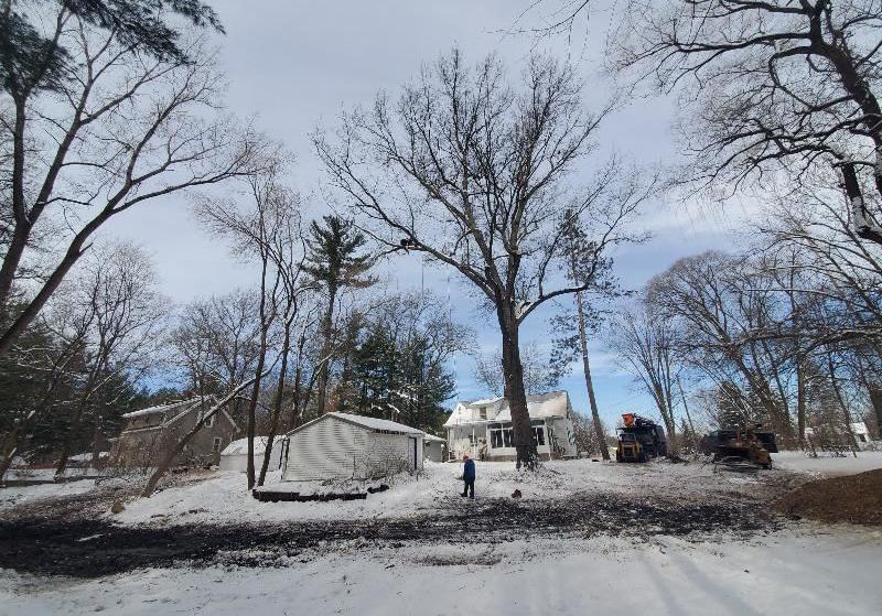 A white house and garage surrounded by fallen snow and barren trees