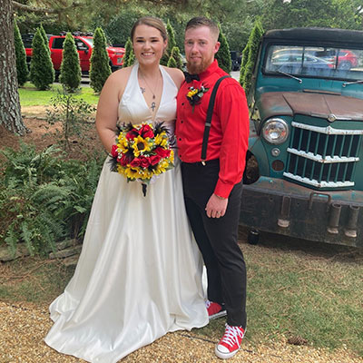 A bride and groom pose for a photo in front of a classic truck.