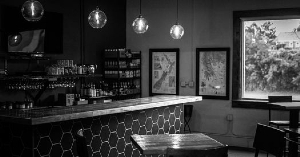 a black-and-white image of a bar, lights hang from the ceiling and framed art adorns the walls
