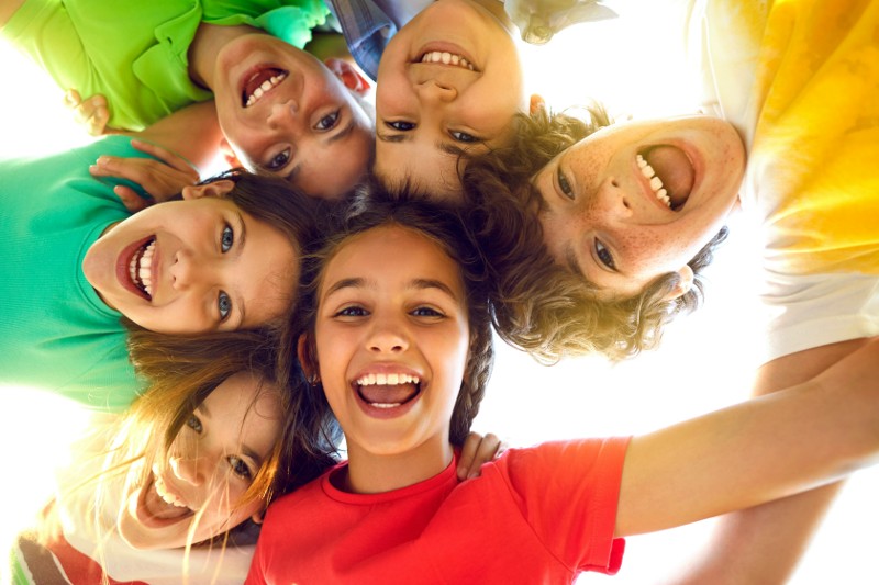 Six young children in a circle put their heads together while looking down at the camera.