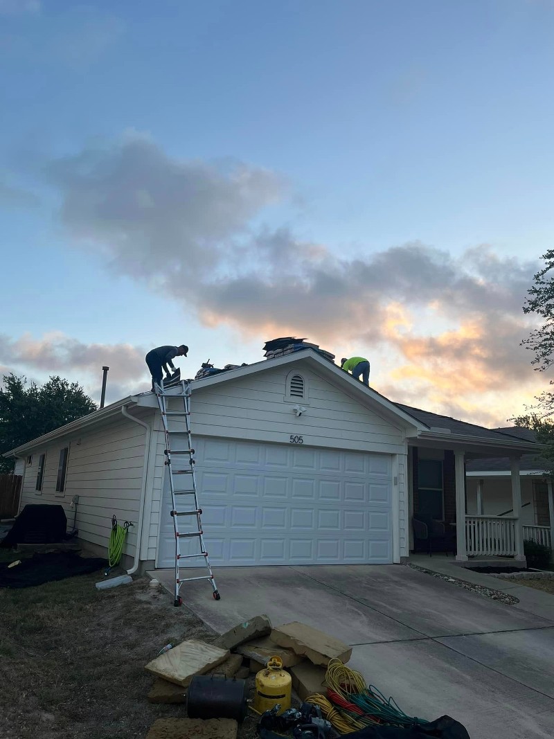 Roofers perform work on the roof of a white garage.