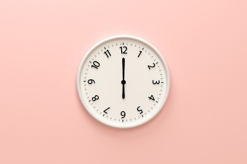 A white clock hangs on a pink wall showing the time as 6 o'clock