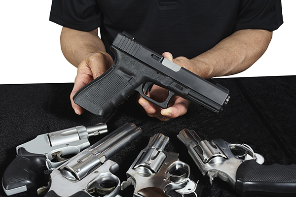Man holding up a gun above other guns on a table