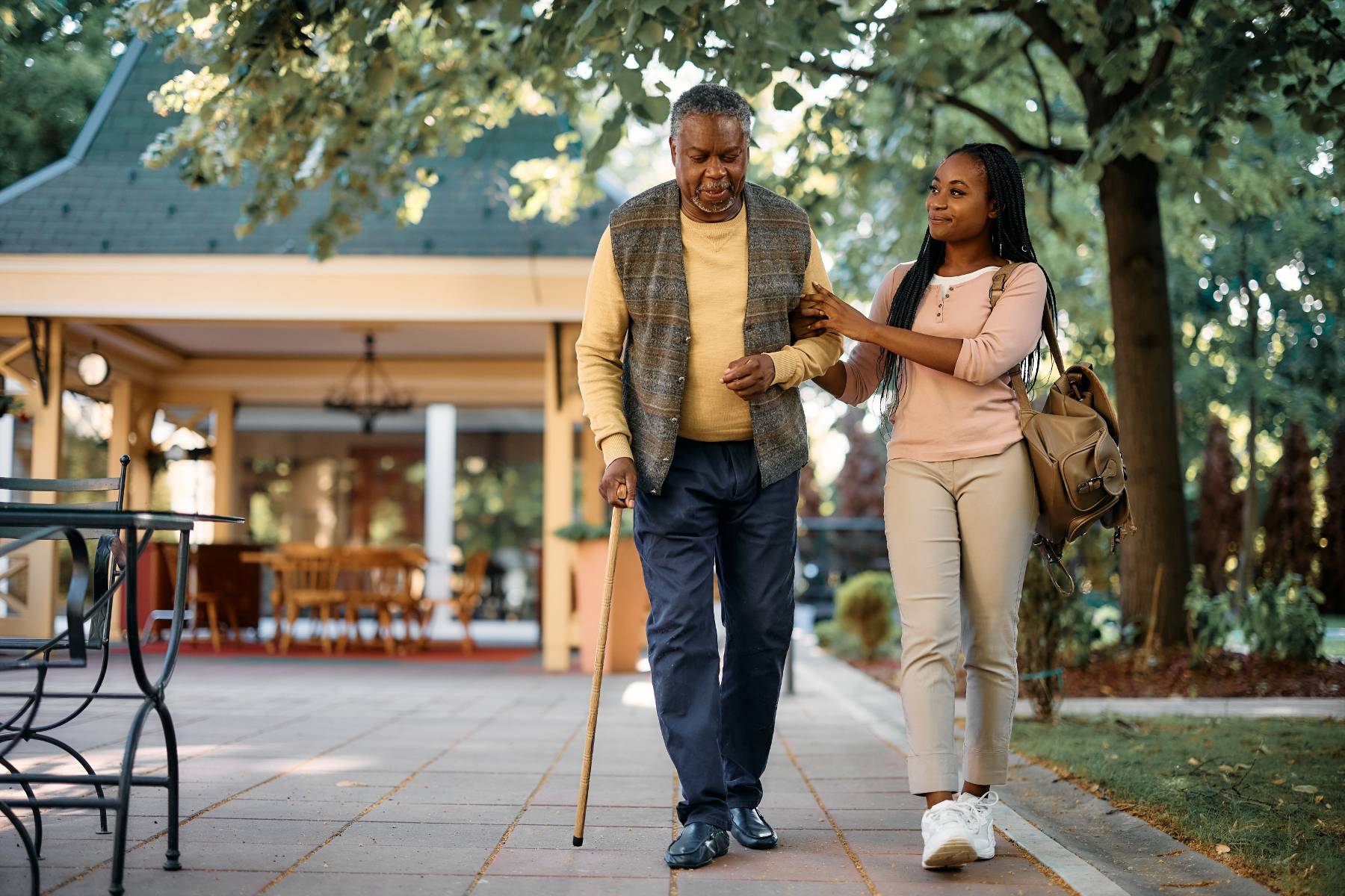 A nurse assists an elderly woman walking with a cane.